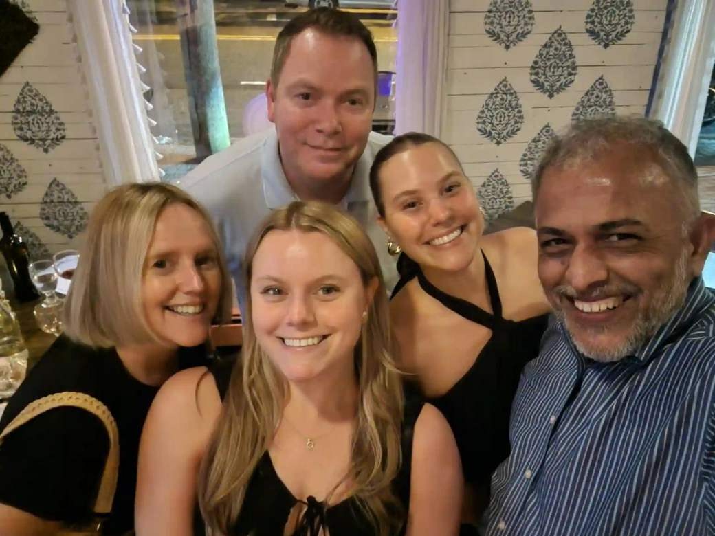 Sonny with four smiling guests at a table in the dining room, block-print wallpaper behind them